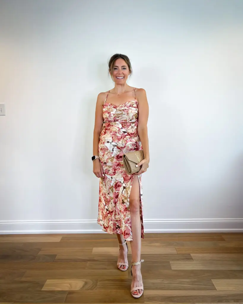 A woman standing in front of a wall wearing a floral dress.