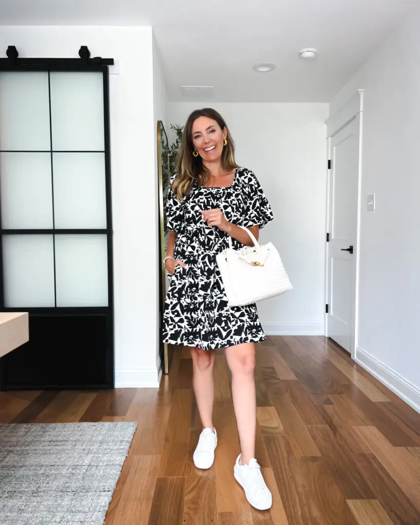 A woman standing in front of a door wearing white sneakers.