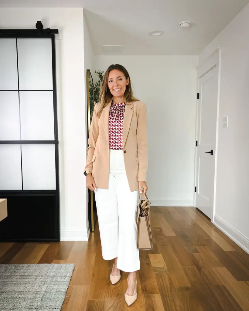 A woman standing in front of a door wearing white pants and a blazer.