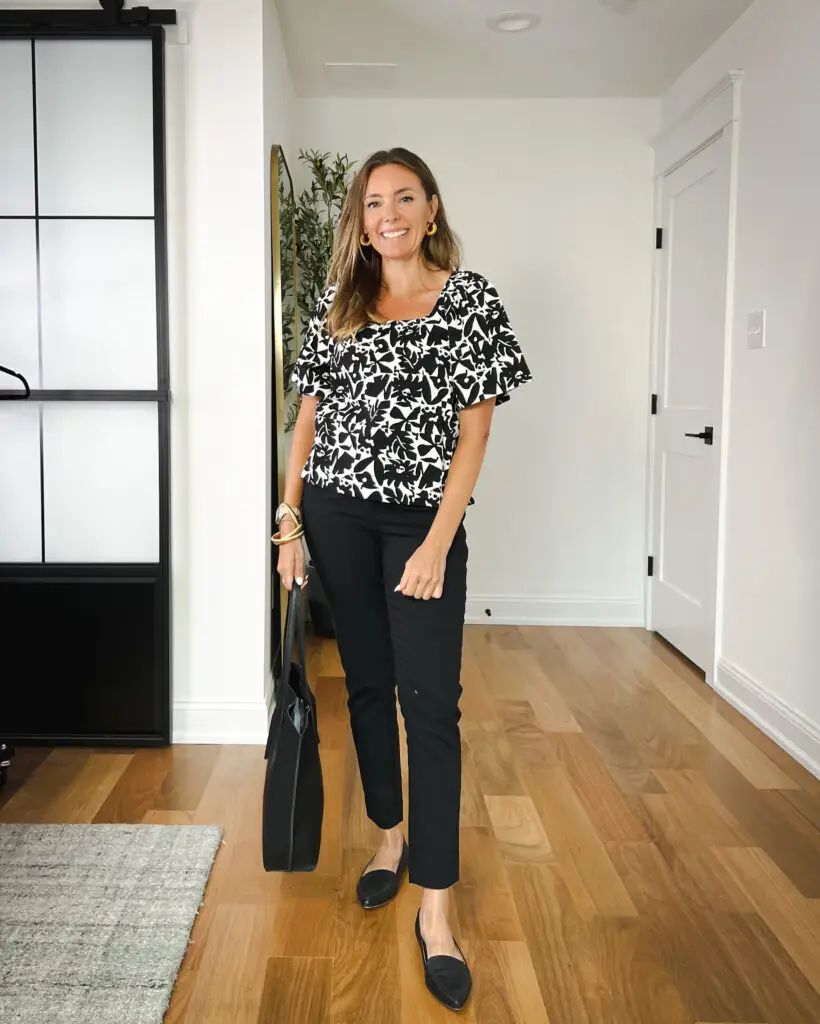 A woman standing in front of a door wearing black pants and a leopard print top.
