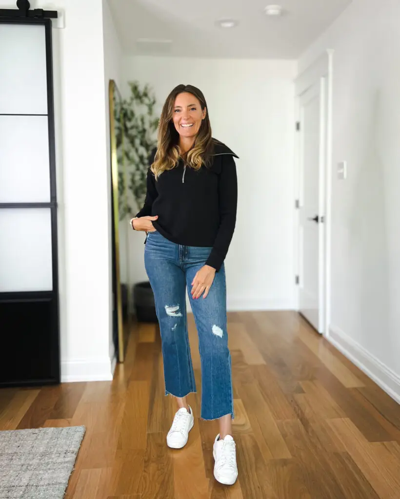 A woman standing in front of a door wearing jeans and sneakers.