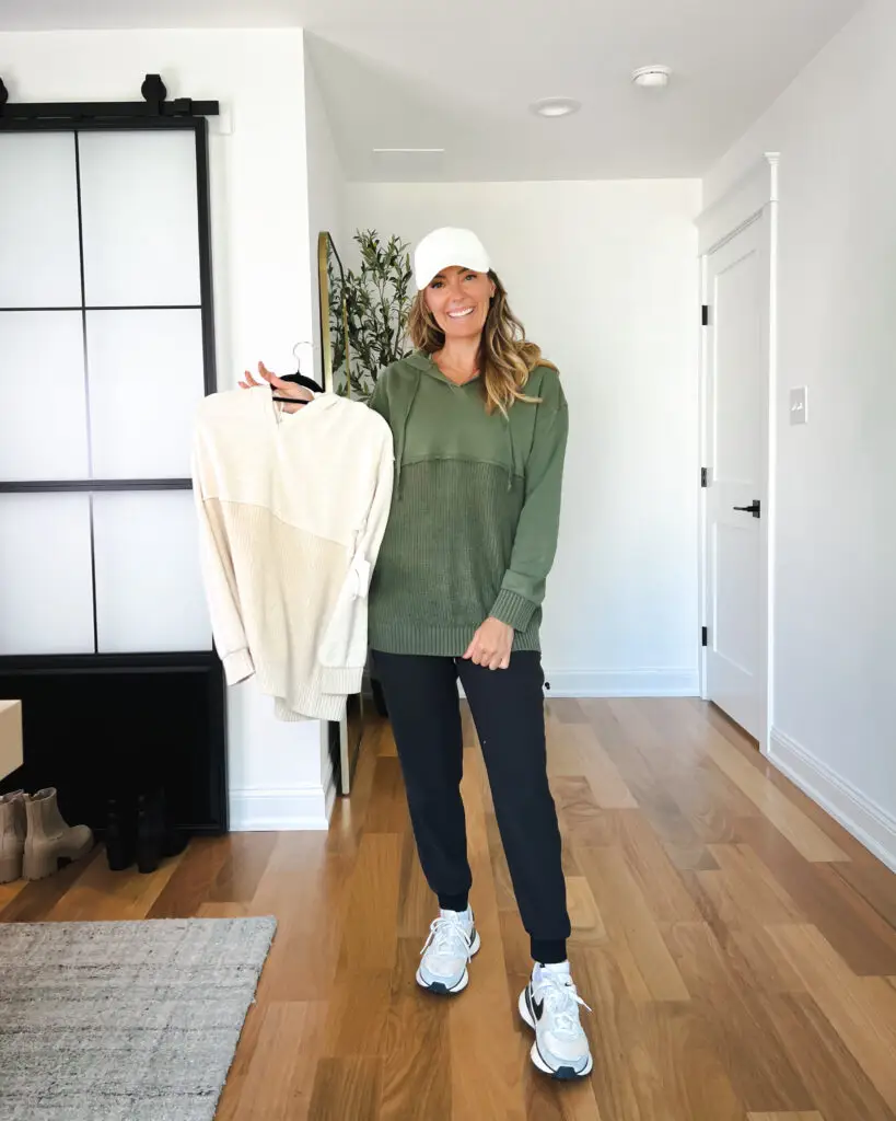 A woman holding up a sweater in her room.