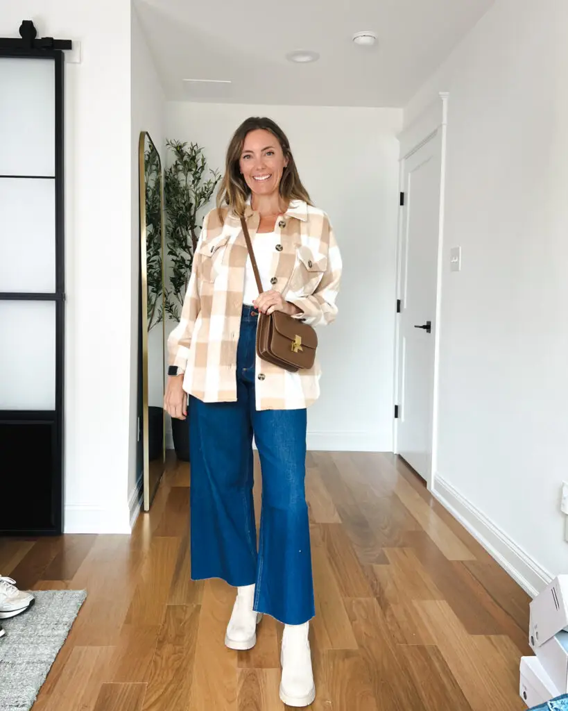 A woman standing in front of a door wearing blue pants.