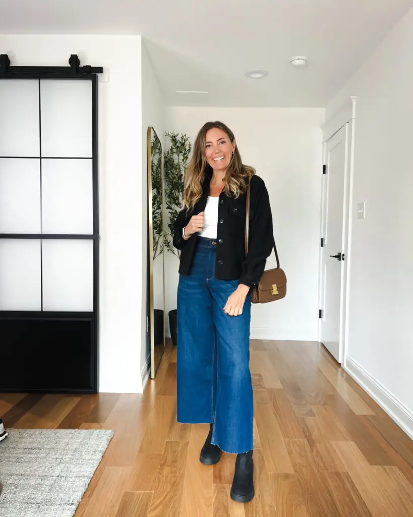 A woman standing in front of a door wearing blue jeans.