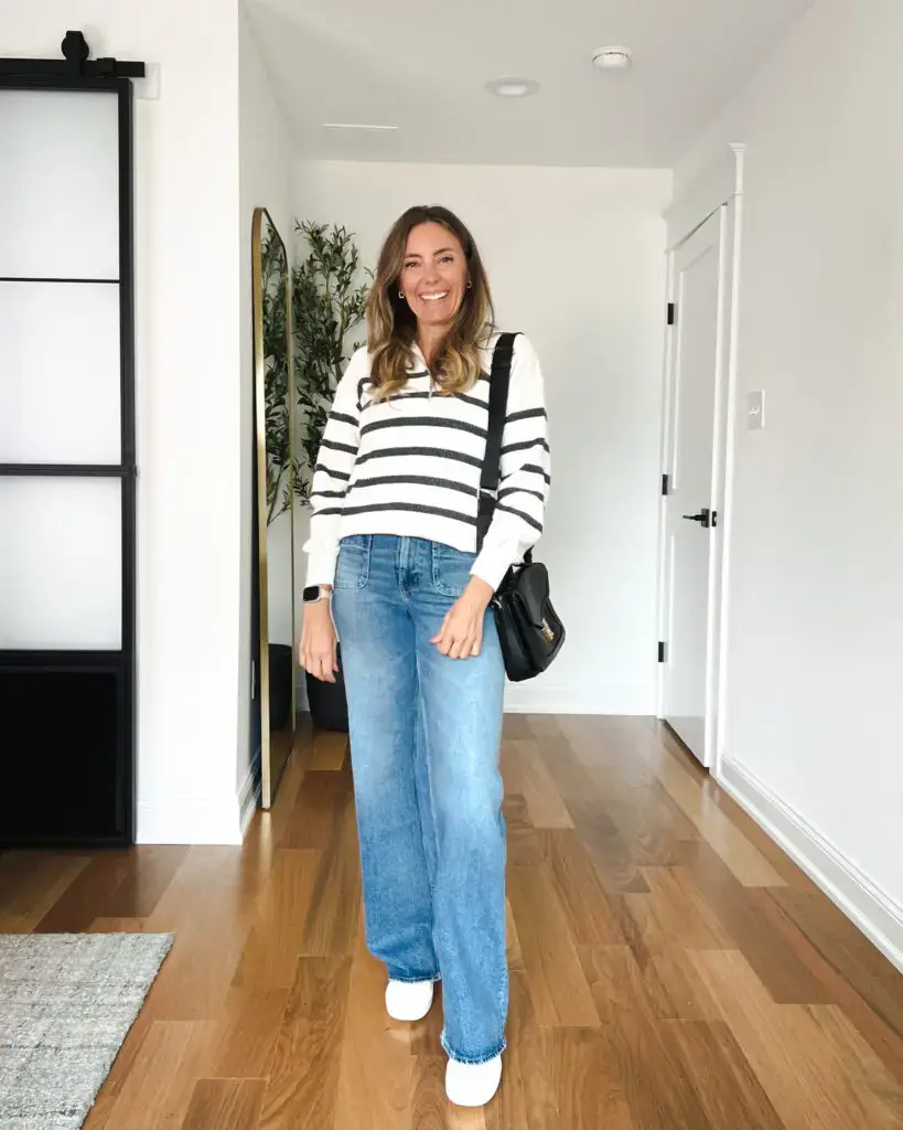 A woman standing in front of a door wearing jeans and a sweater.
