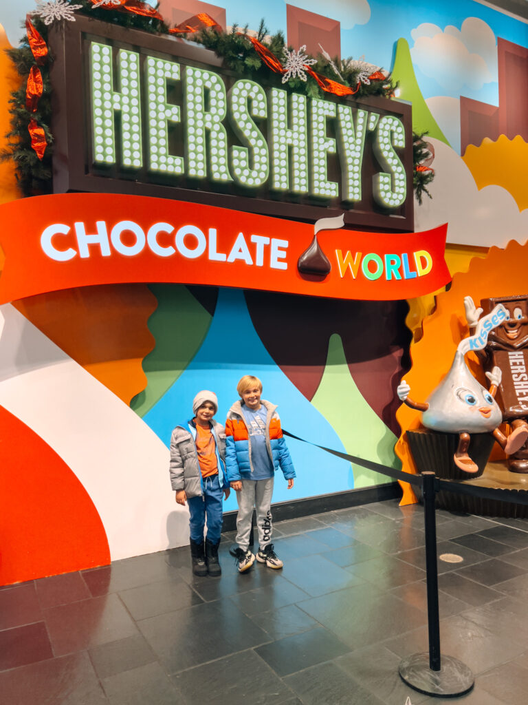 Two kids standing in front of a chocolate world sign.