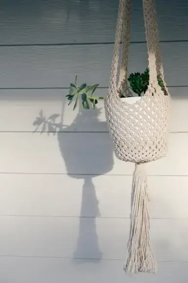 Boho Macrame Planter for Outdoor - Sweet Motherly White macrame hanging planter with succulents casting a shadow on white siding.