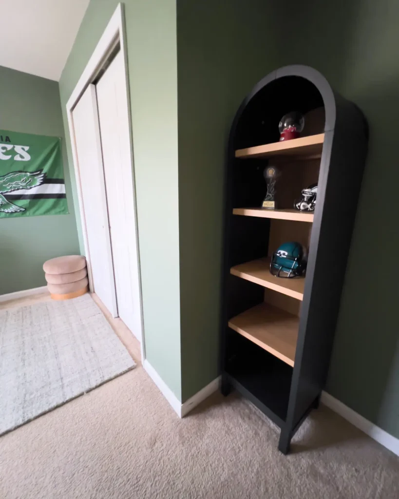 Black arched bookshelf with Eagles helmet, trophy, and collectibles in green sports-themed boys bedroom.