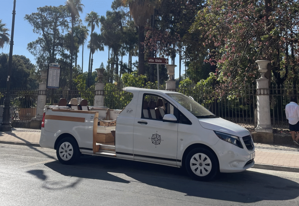 CruiserCar Tour Stop at Villa Giulia in Palermo - Sweet Motherly CruiserCar tour vehicle parked in front of Villa Giulia in Palermo, with passengers seated inside under palm trees.