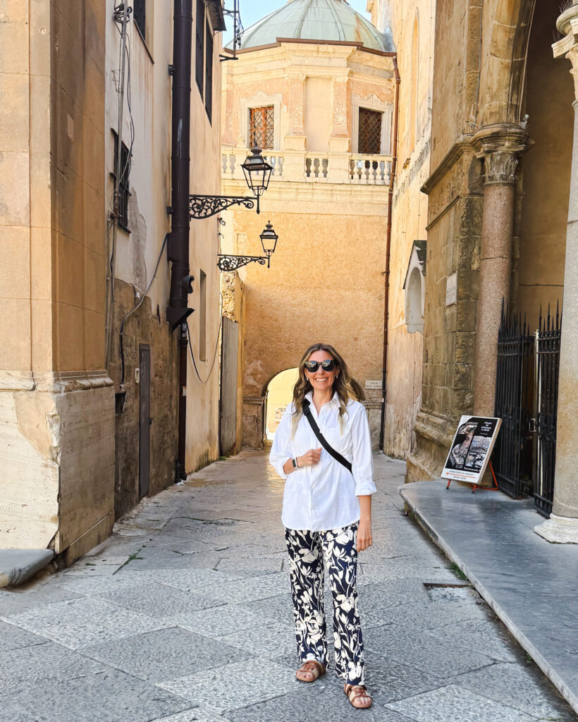 Woman in Golden Alleyway in Palermo’s Historic Center - Sweet Motherly Woman standing in a quiet historic alleyway in Palermo, Sicily, with domed buildings and golden architecture behind her.