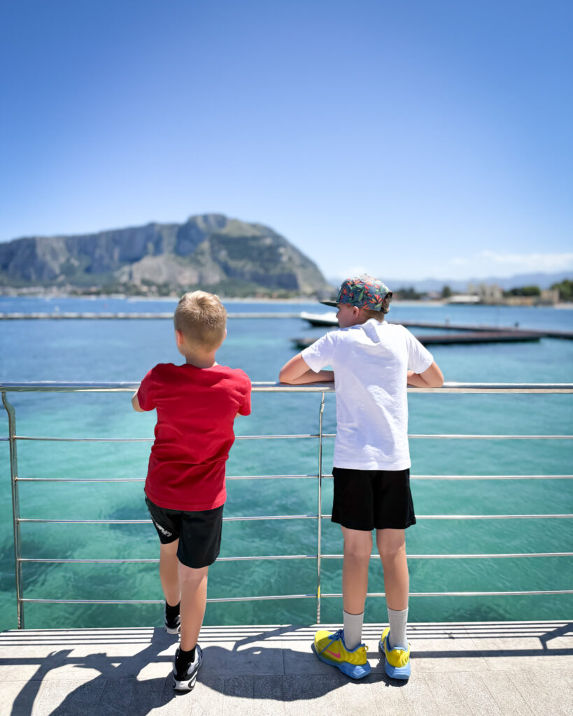 Boys Overlooking Palermo’s Turquoise Coastline - Sweet Motherly Two boys looking out over the turquoise waters and rocky coastline of Palermo, Sicily.