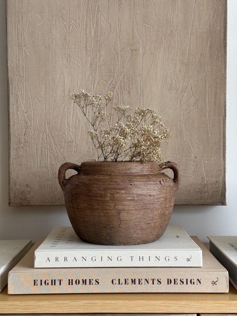A rustic ceramic vase with dried florals styled on stacked design books, blending natural textures with minimal styling.