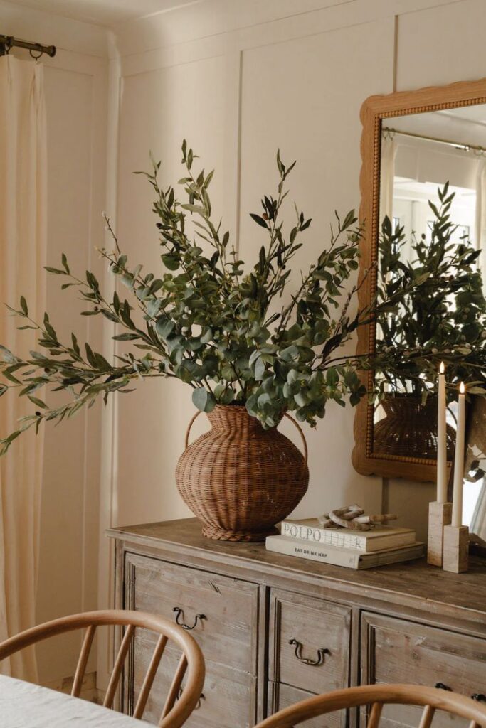 A rustic wooden buffet styled with a wicker vase filled with olive branches, paired with neutral books and candles.
