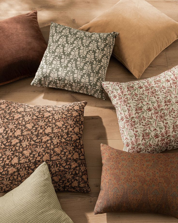 A collection of fall-toned pillows in earthy rust, moss, and neutral shades with subtle patterns and textures.