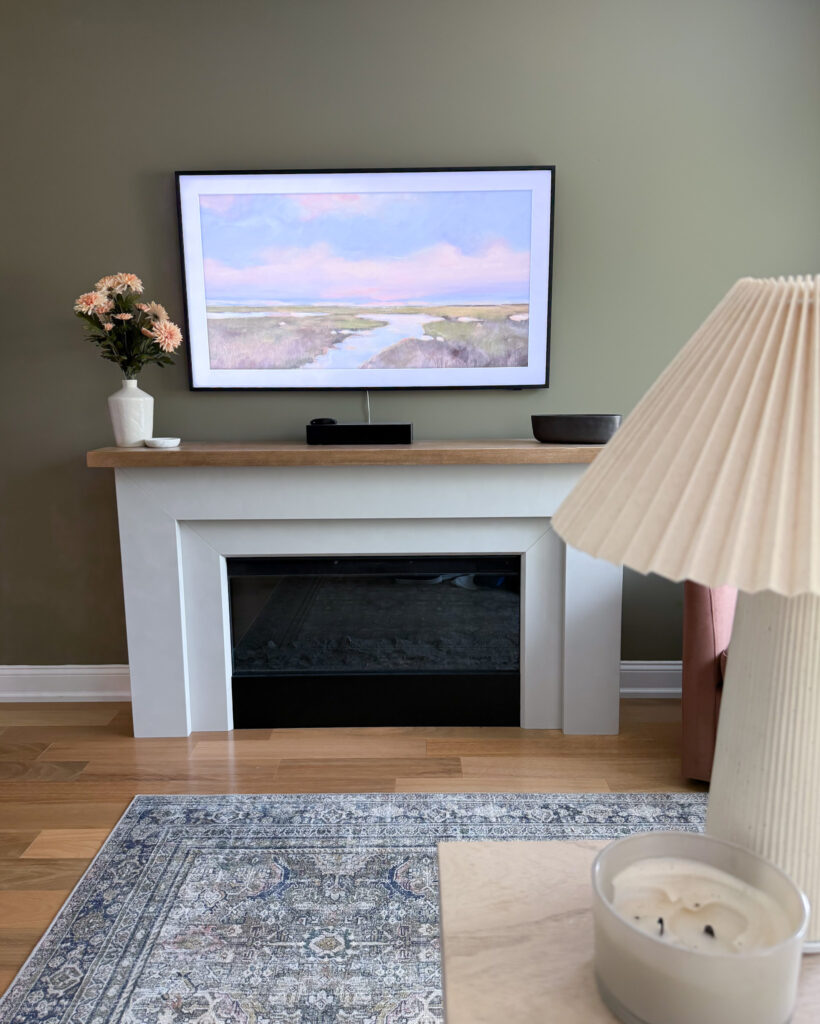 Frame TV showing artwork above fireplace, with lamp and rug in view.