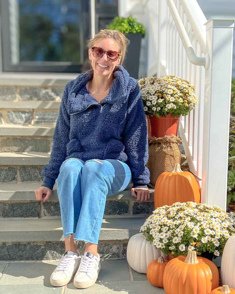 Women sitting by warm fall porch decor with pumpkins, white mums, and a cozy layered look on front steps.