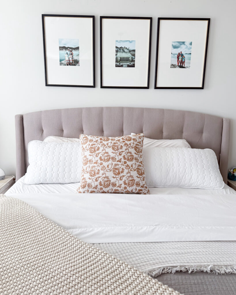 A cozy, modern bedroom with a tufted bed, neutral bedding, and three framed abstract art prints that tie in with the soft pink curtains.