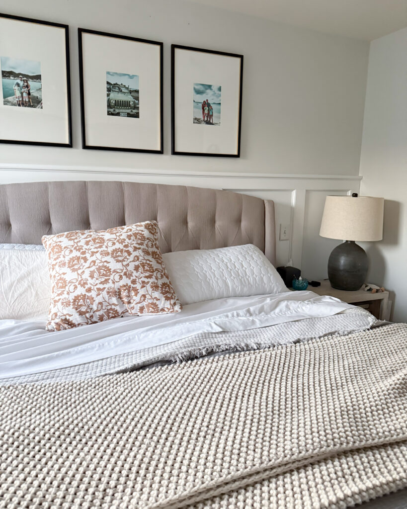 A bright, inviting view of the bed with a tufted headboard, white linens, beige throw blanket, and patterned pillow adding a subtle pop of warmth.