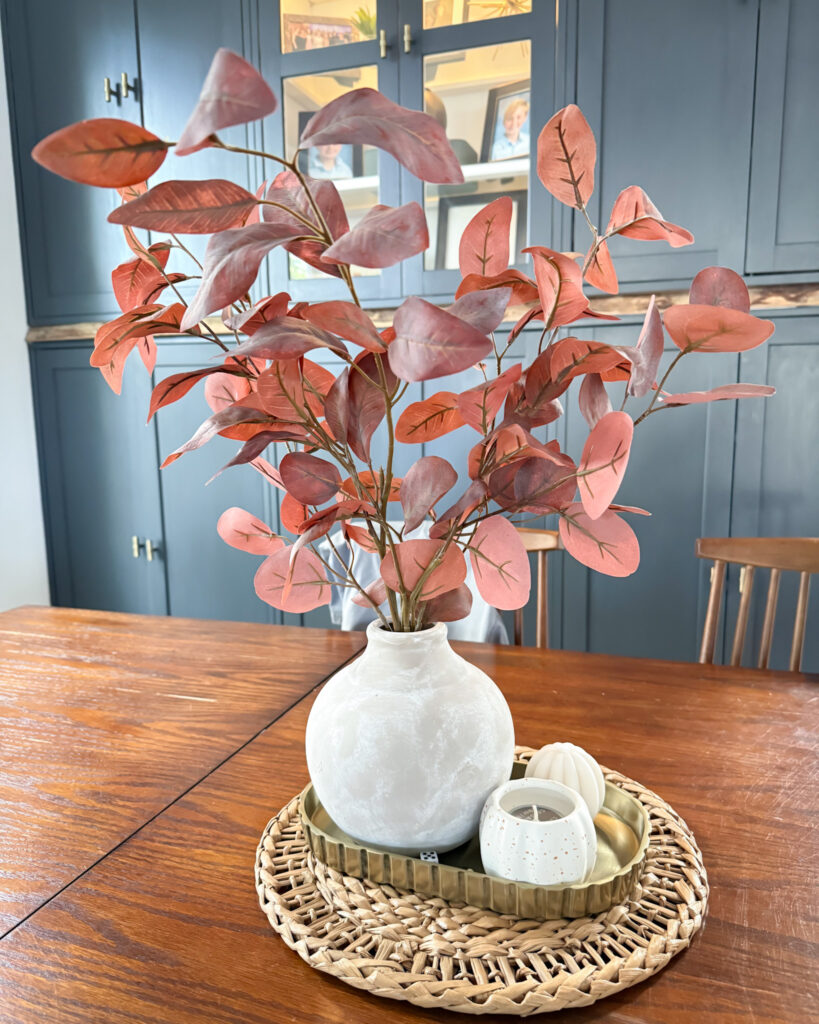 IMG_4361 - Sweet Motherly White vase with rust-colored fall stems and small pumpkins on woven tray centerpiece on dining table