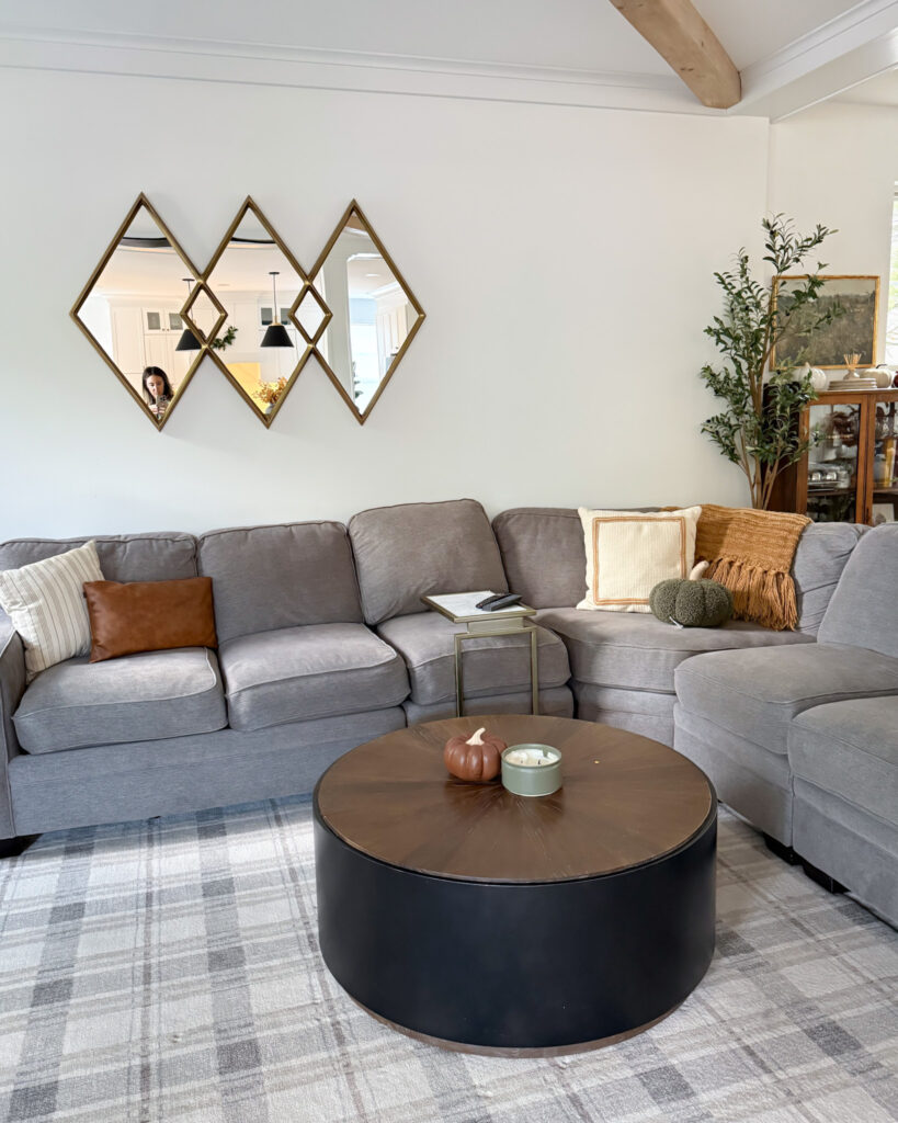 IMG_4412 - Sweet Motherly Neutral living room with plaid area rug, round wood coffee table, and gray sectional sofa styled for fall decor
