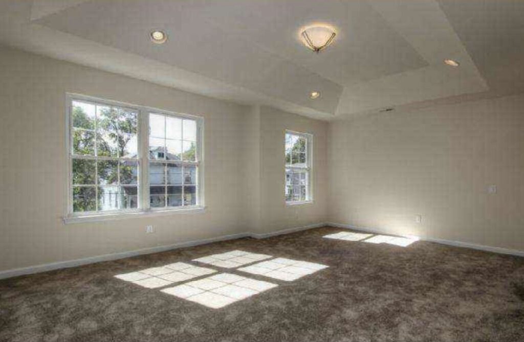 A wide view of the empty space showing the doorway to an adjoining room and soft sunlight on the carpet.