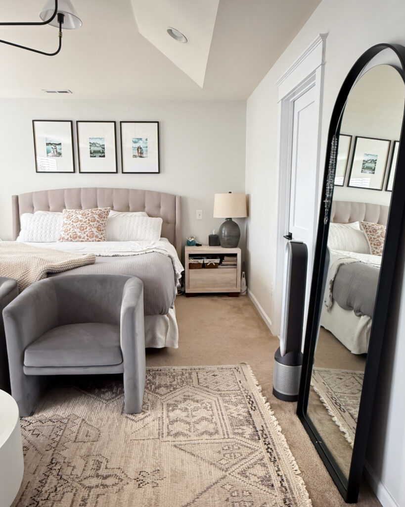 A wider view of the room featuring a beige patterned rug, gray chairs, and a tall black floor mirror reflecting the light from the windows.