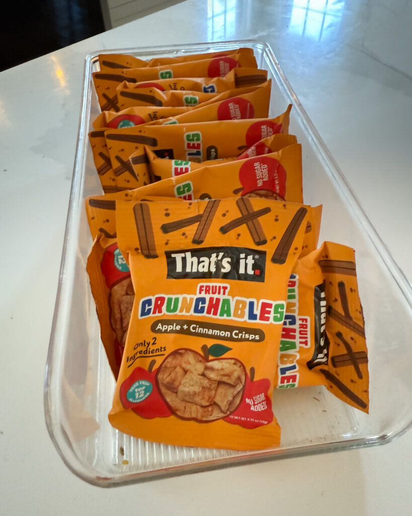 Clear kitchen bin organizing grab-and-go snacks inside a pantry cabinet.