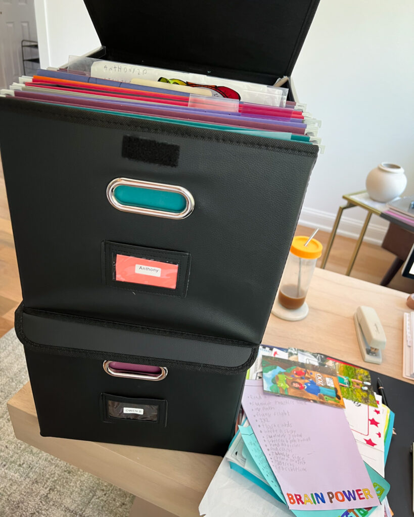 Labeled storage bins organizing kids’ artwork and school papers.