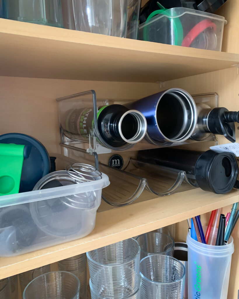 Kitchen cabinet with shelves organizing cups, bottles, and pantry items.