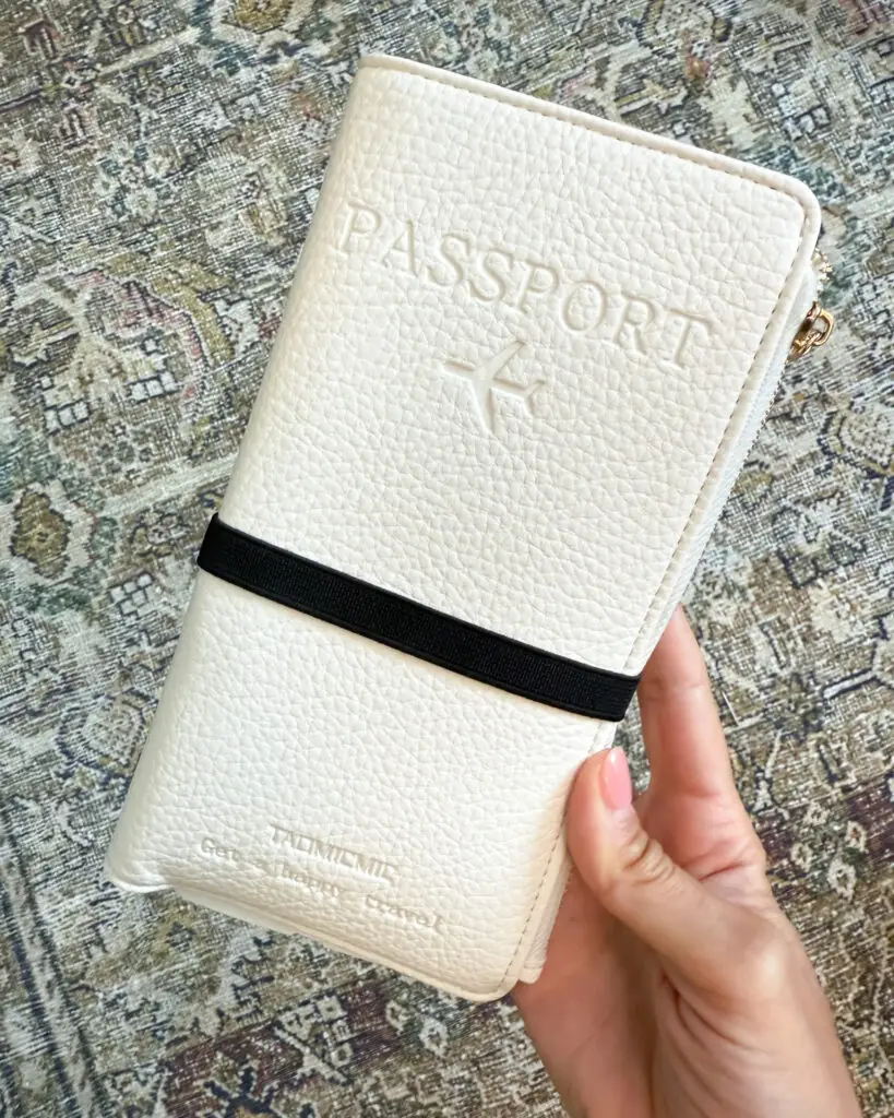 IMG_1409 - Sweet Motherly Cream textured passport holder with black elastic band held in hand on patterned rug – stylish Cruise Essentials from Amazon for organized travel documents.