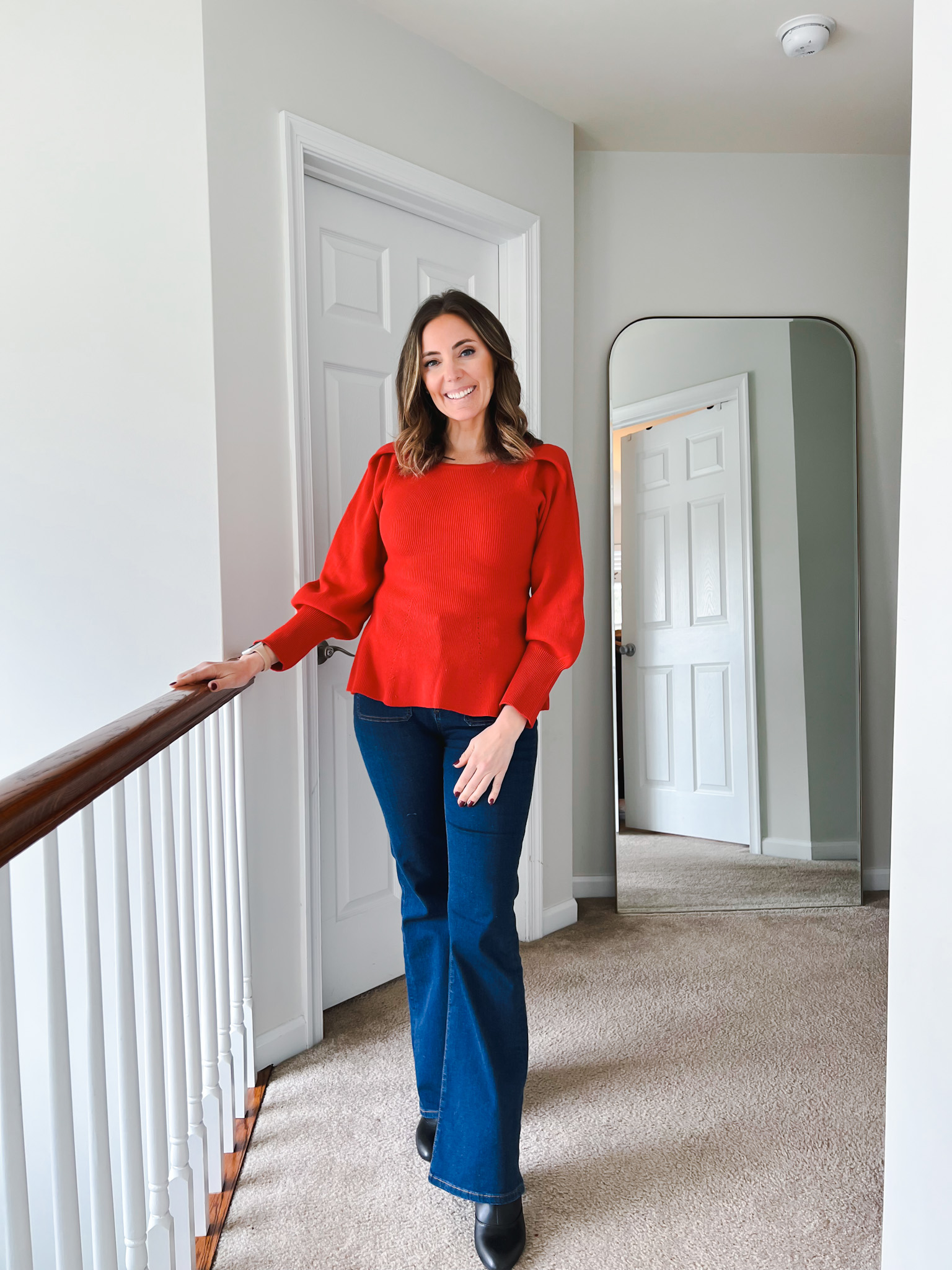 Woman wearing a bright red puff sleeve sweater paired with dark flare jeans and black ankle boots for a chic Valentine’s Day outfit.
