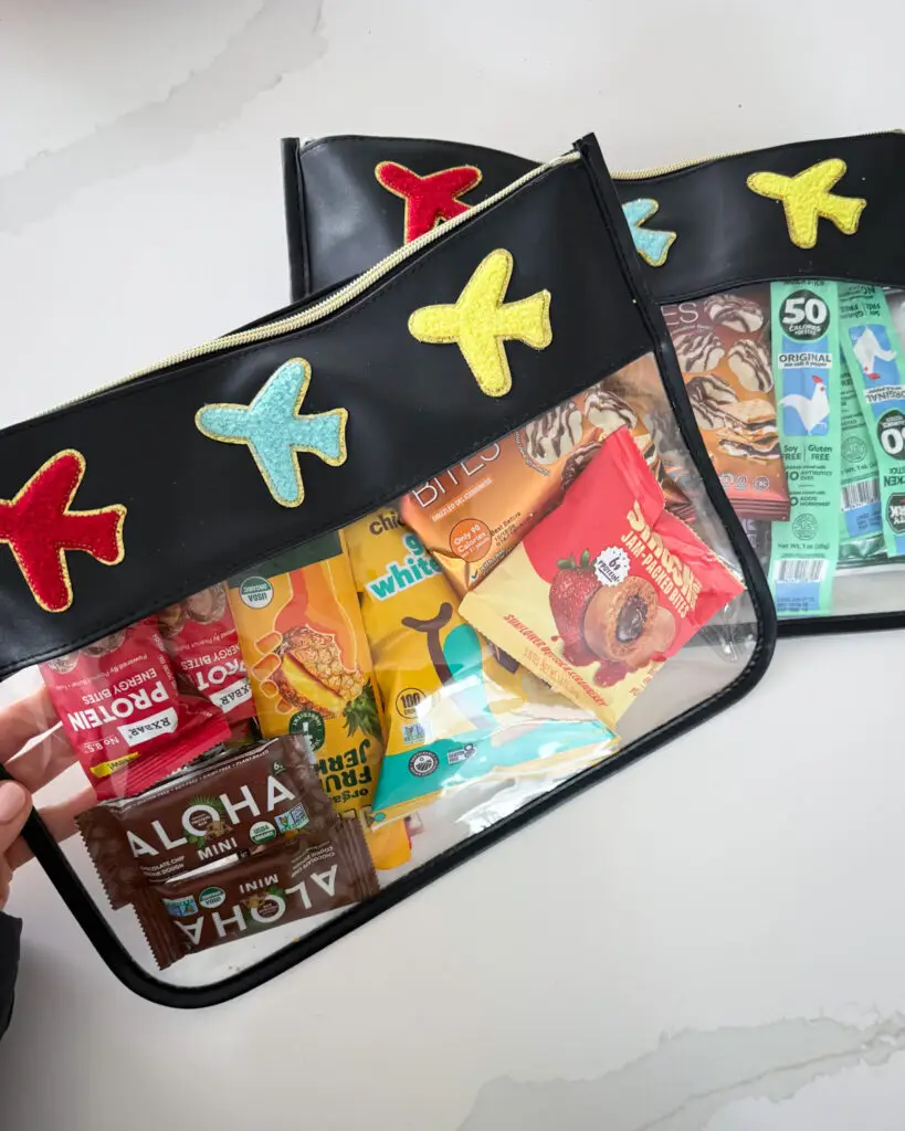 Clear airplane-themed travel snack pouch filled with snacks, a smart family travel essential from Amazon for keeping kids organized on flights.