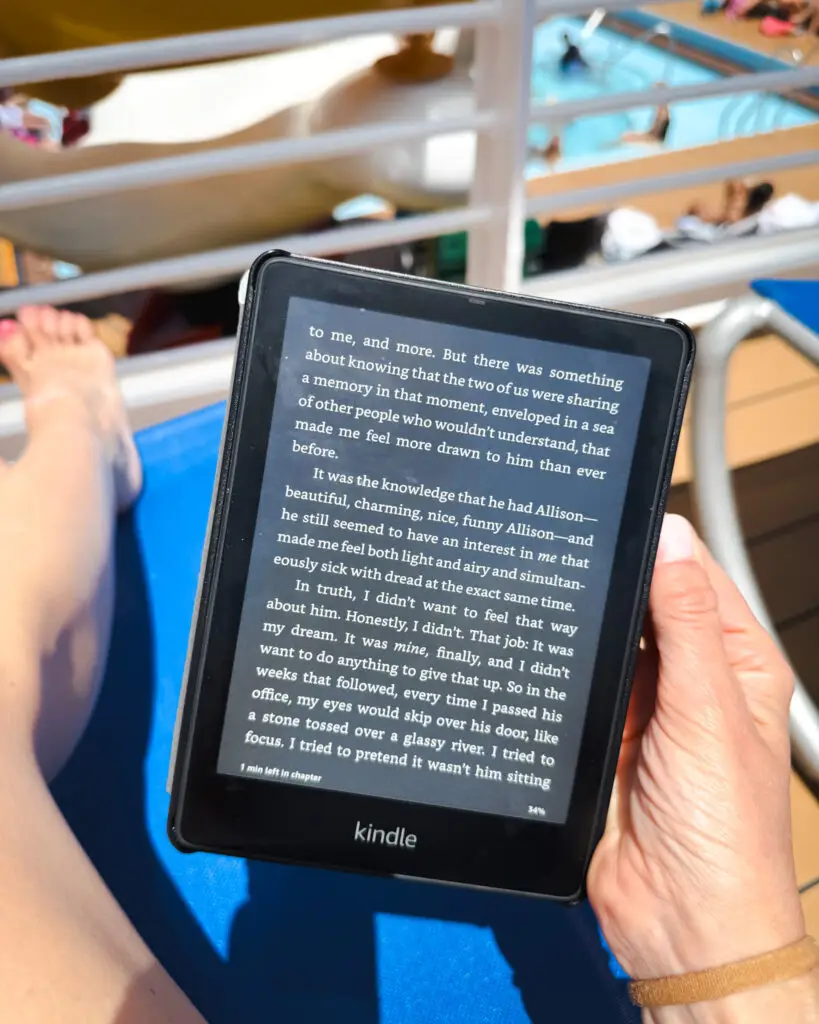 IMG_8763 - Sweet Motherly Kindle e-reader held poolside on cruise ship deck with water slide and pool in background – relaxing Cruise Essentials from Amazon.