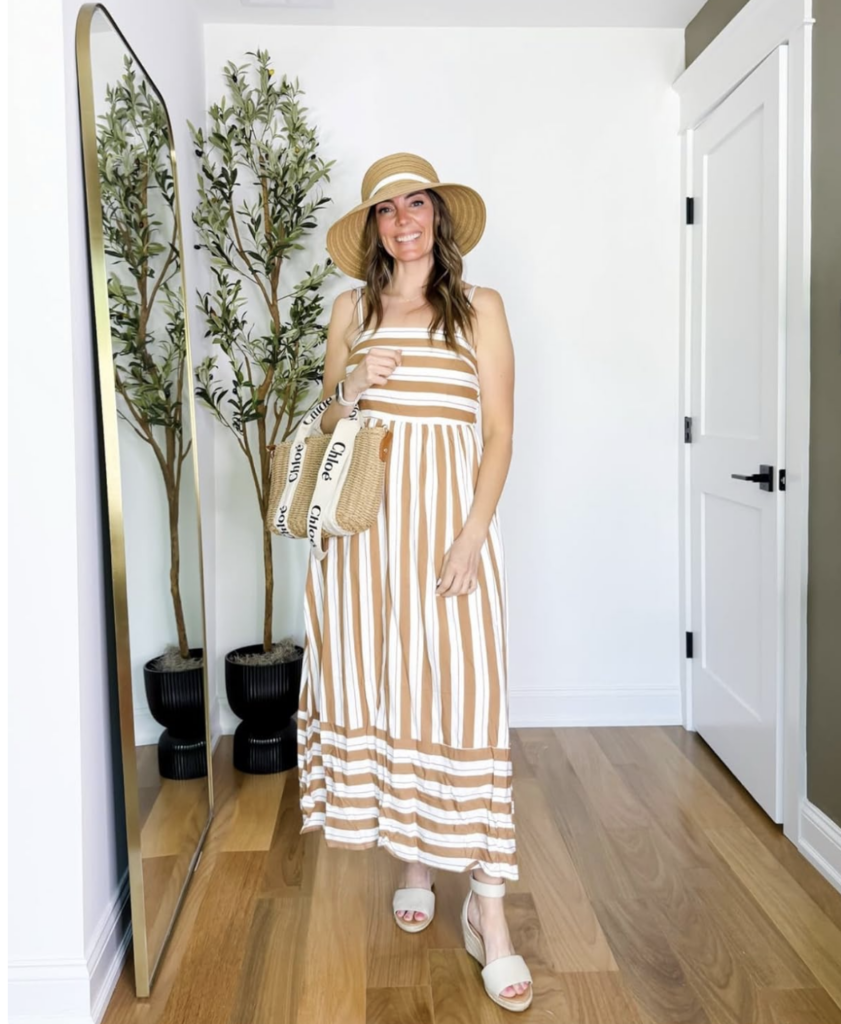 Screenshot 2026-02-02 at 100519 AM - Sweet Motherly Woman wearing a tan and white striped maxi dress with a straw sun hat, woven tote bag, and neutral wedge sandals for chic and comfortable resort styling.