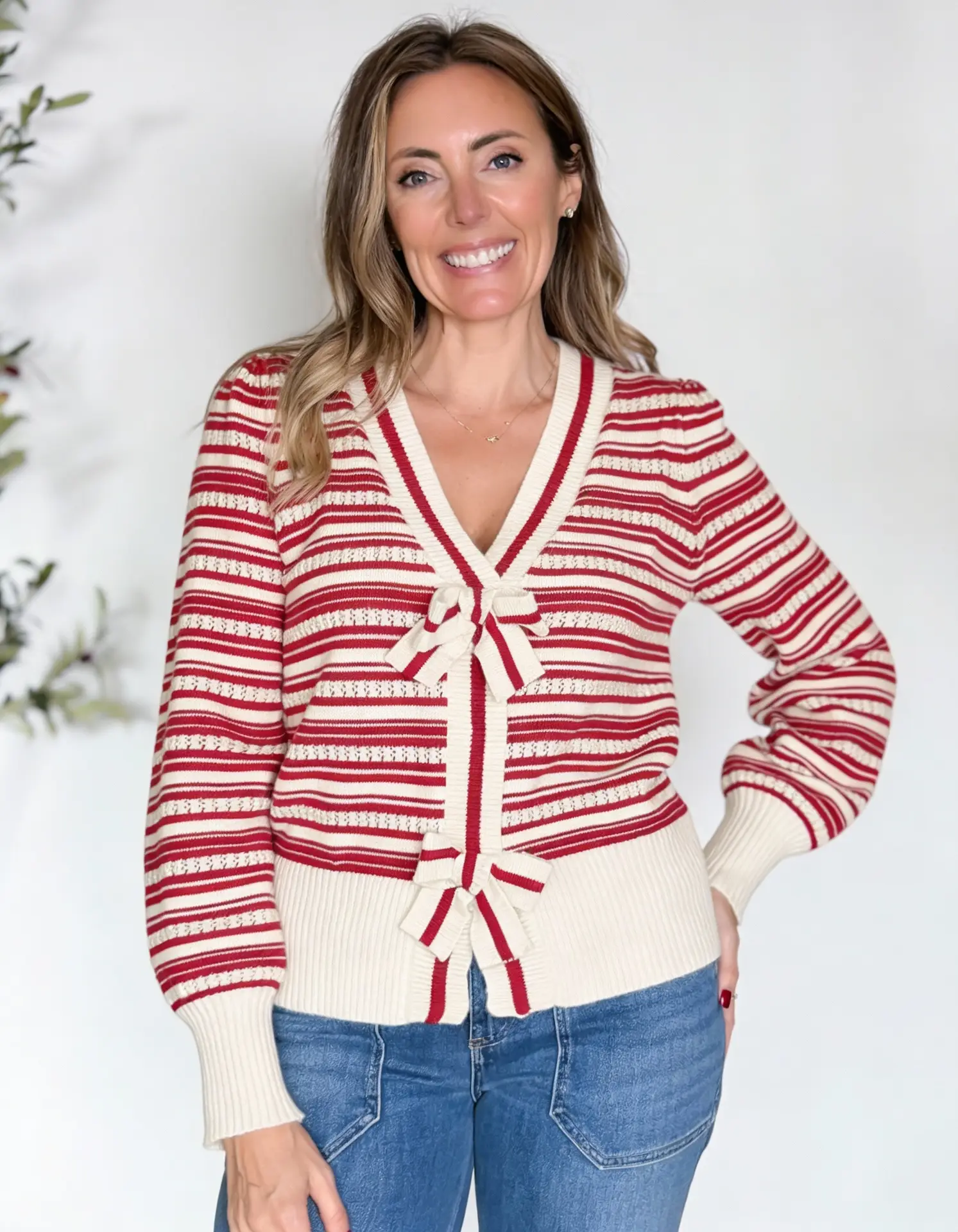 Woman wearing an affordable red and white striped cardigan with bow details styled with blue jeans for a casual Valentine’s Day outfit.