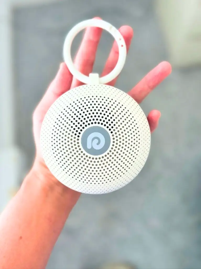 Small white noise machine with loop handle held in hand, a compact family travel essential from Amazon for music on the go.