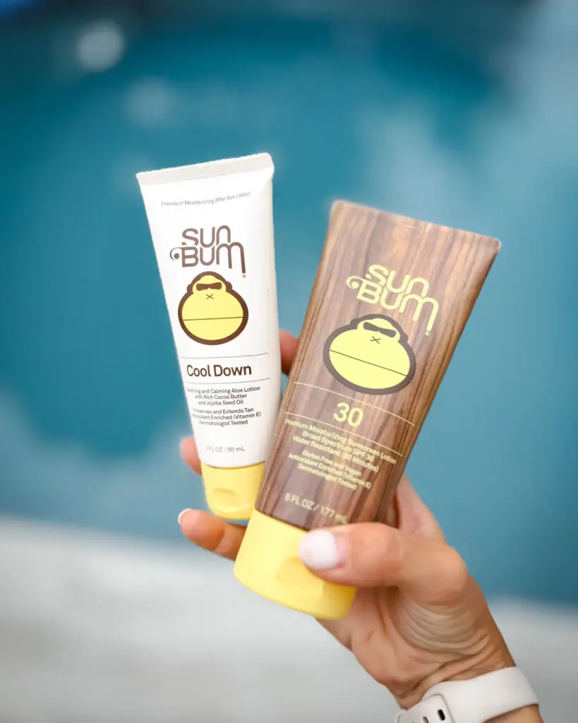 Hand holding Sun Bum SPF 30 sunscreen and after sun cooling lotion by a pool, essential sun protection for family travel from Amazon.