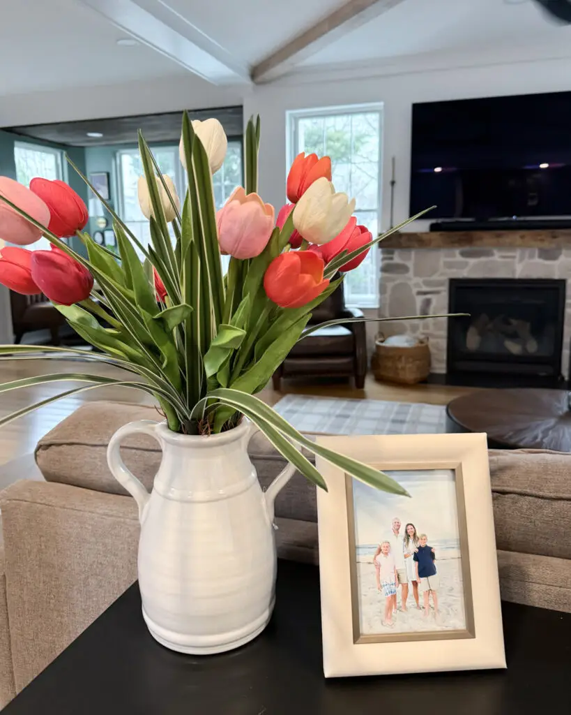 White ceramic vase with pink and white tulips next to a framed family photo on a console table