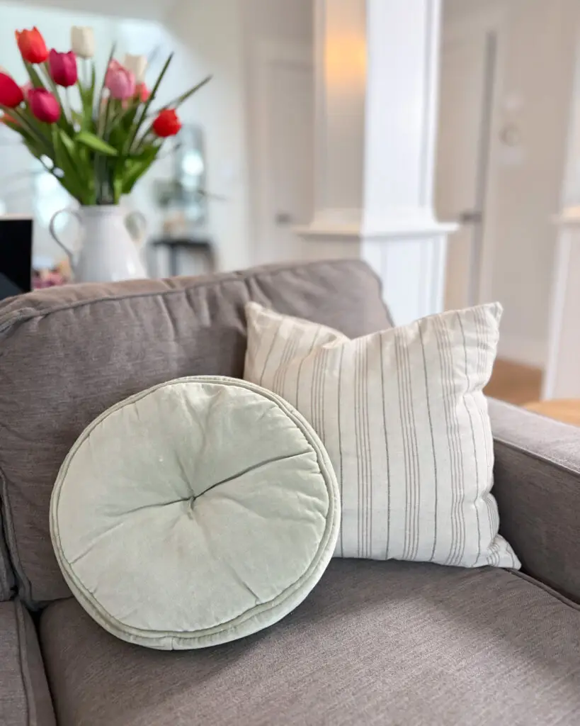 Neutral living room couch styled with soft green round pillow and striped accent pillow