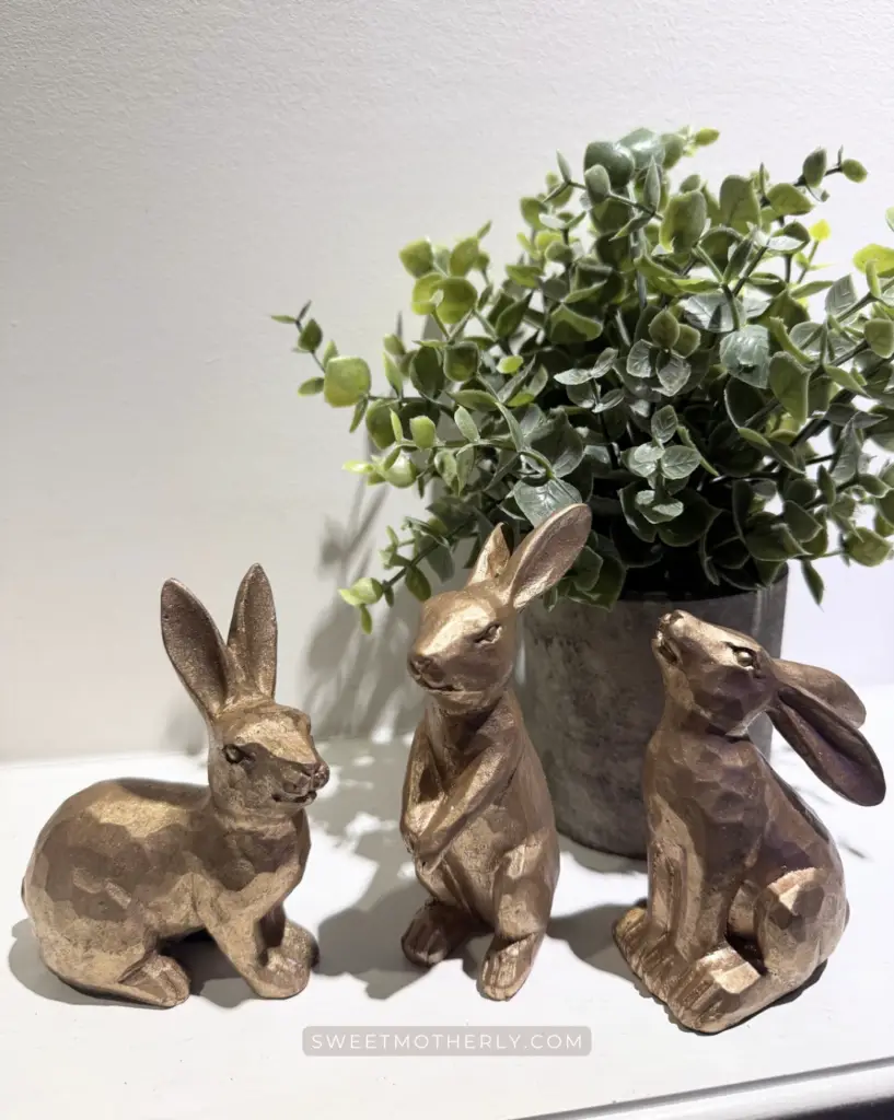 Gold bunny figurines with faux greenery in a neutral pot on a white shelf, spring home decor styling. Simple spring home decor.