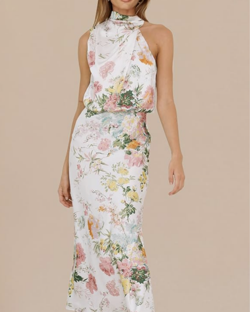 Woman wearing a white floral halter-neck maxi dress with pink, yellow, and green blooms on a neutral backdrop, full-length view on model.